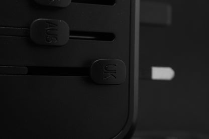 Close-up van de ELEKSO adapter met duidelijk zichtbare UK en AUS schuifknoppen voor internationale compatibiliteit.