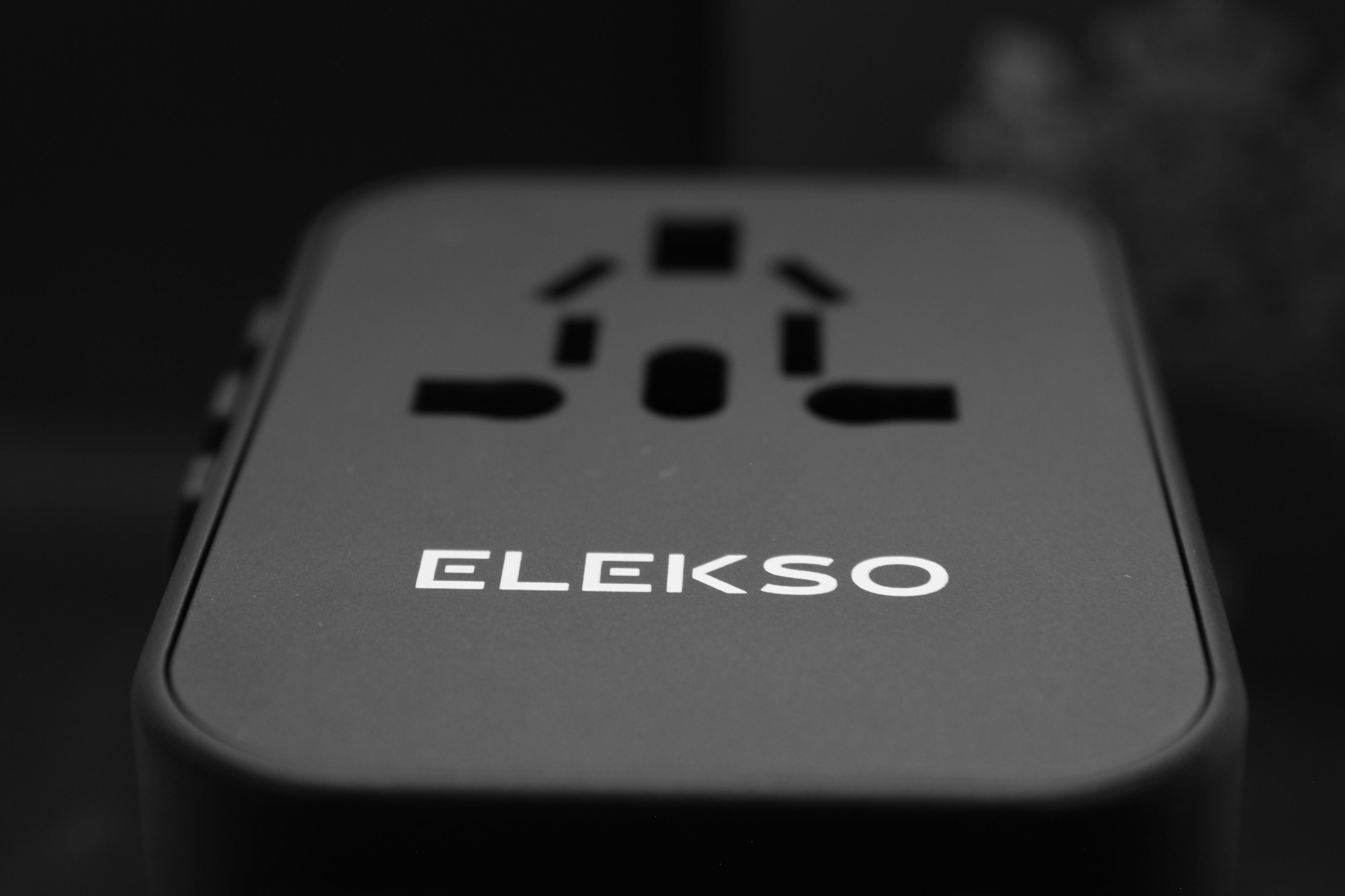 Hoekperspectief van de ELEKSO reisadapter met logo in beeld en internationale invoeropeningen.