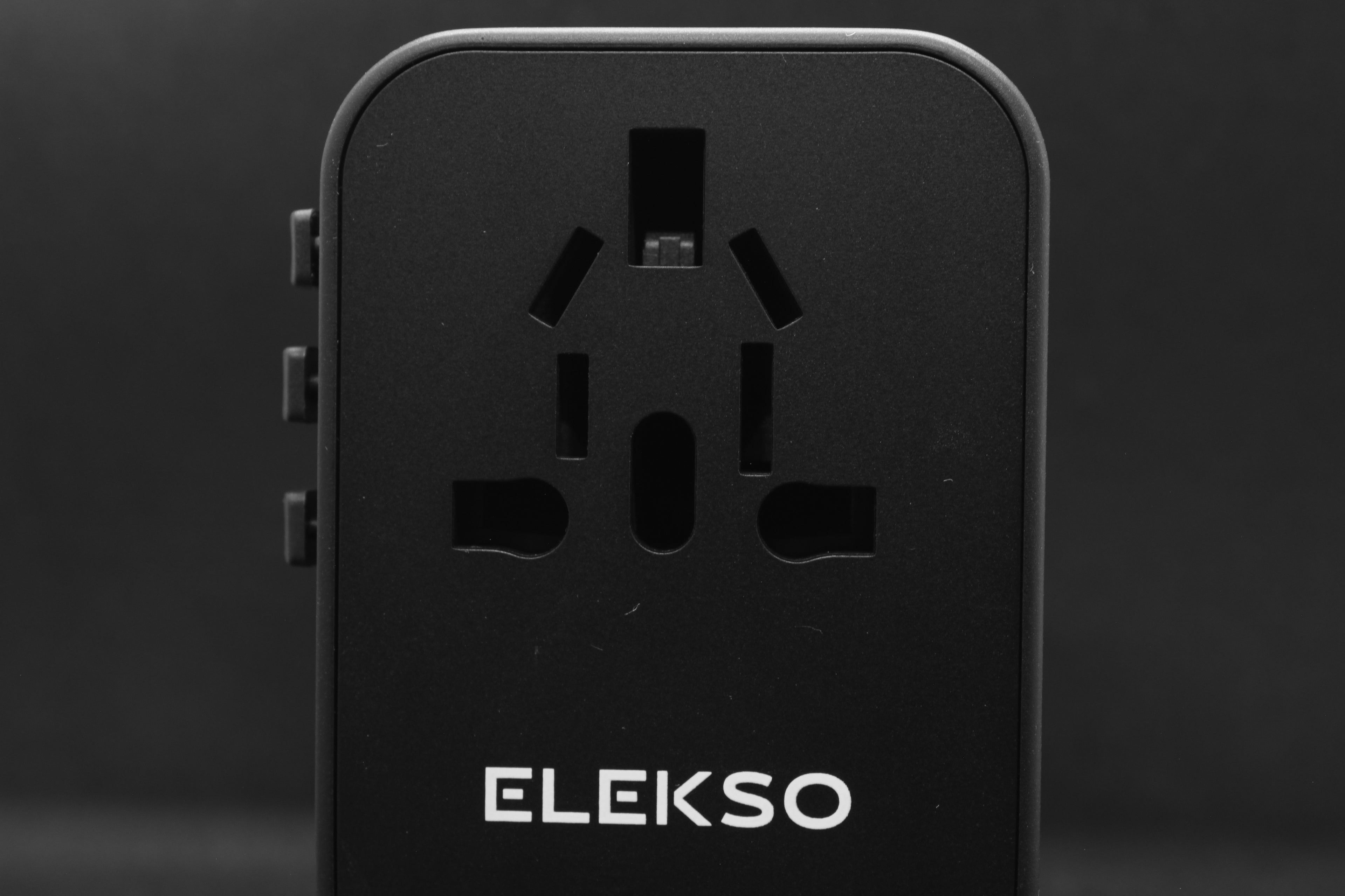 Vooraanzicht van de ELEKSO wereldstekker, geplaatst voor een paspoort — ideaal voor reissituaties.