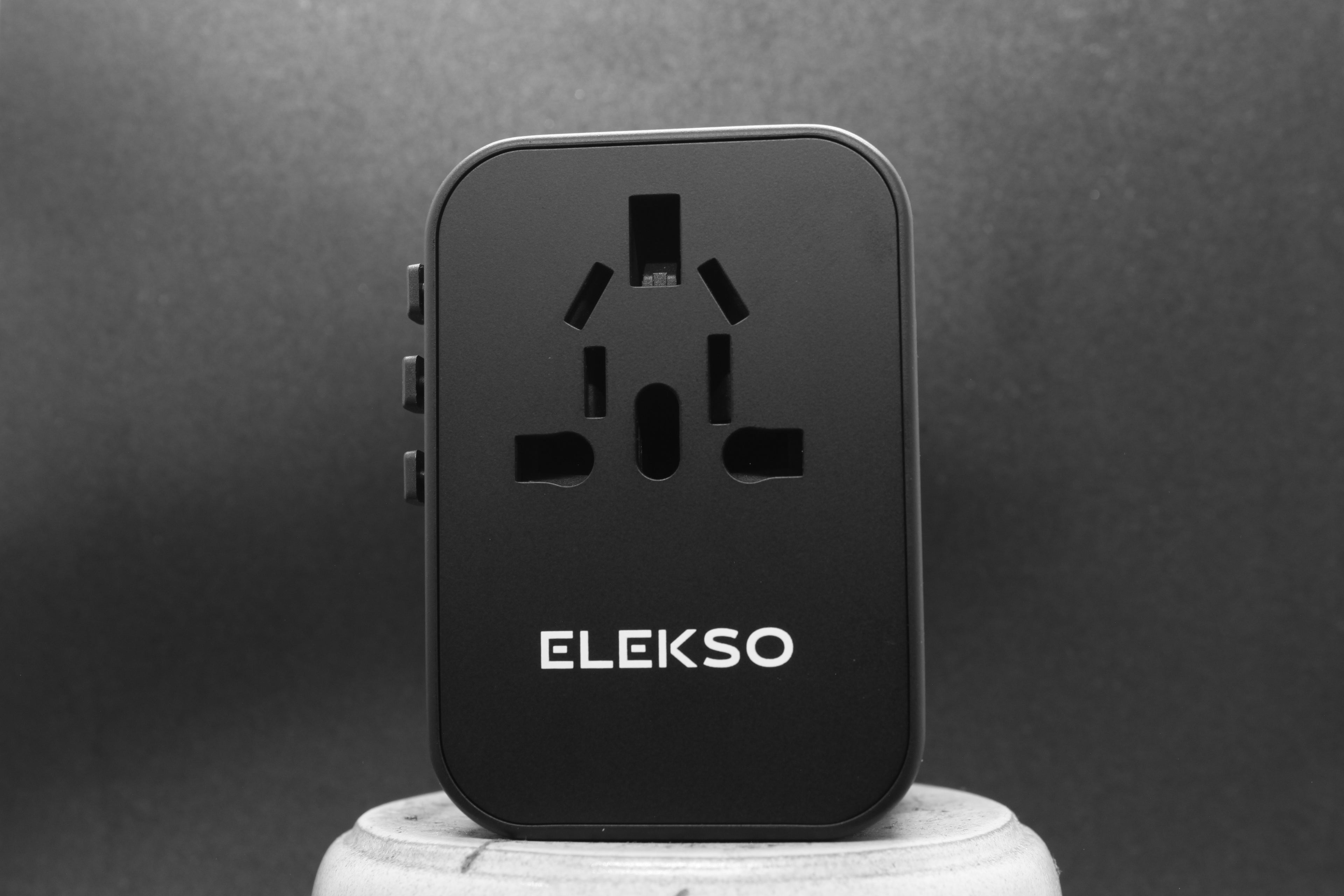 Vooraanzicht van de ELEKSO universele reisstekker met internationaal invoerpatroon en compact ontwerp.